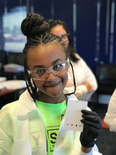smiling student in the lab with eye goggles and test results