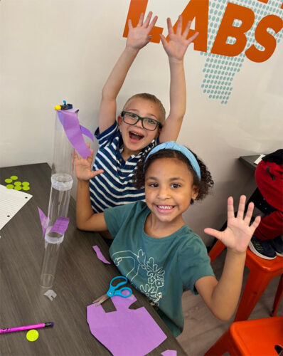 first graders working on engineering design challenge showing happy hands!