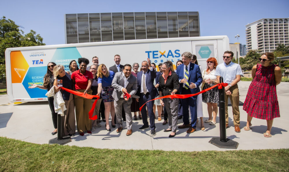 a group of people cutting a red ribbon in front of a mobile laboratory